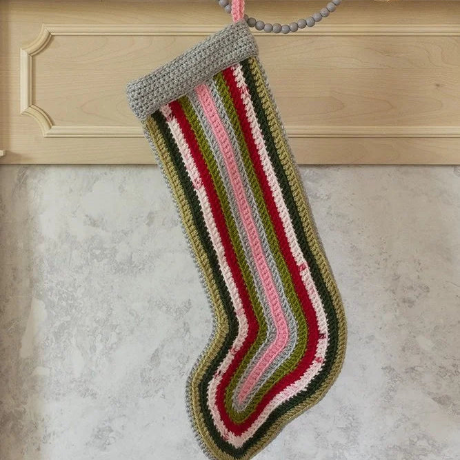 Colorful striped crochet Christmas stocking hanging on a fireplace mantle.
